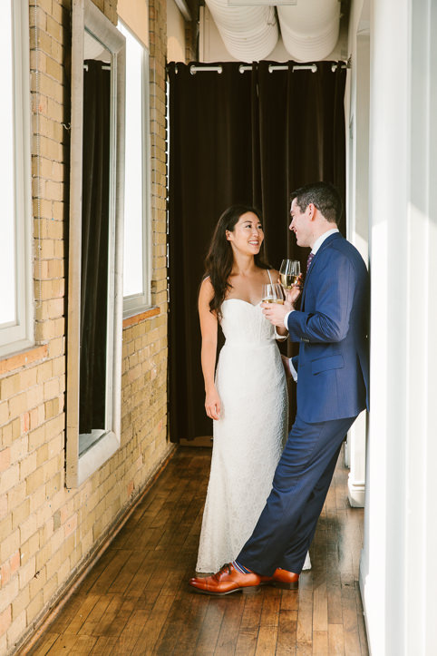 A bride and groom share a glass of wine in a hallway at their Spoke Club wedding in Toronto.
