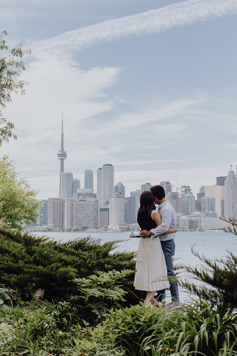 Couple embracing during Wars Island engagement session while looking towards a view of the Toronto skyline