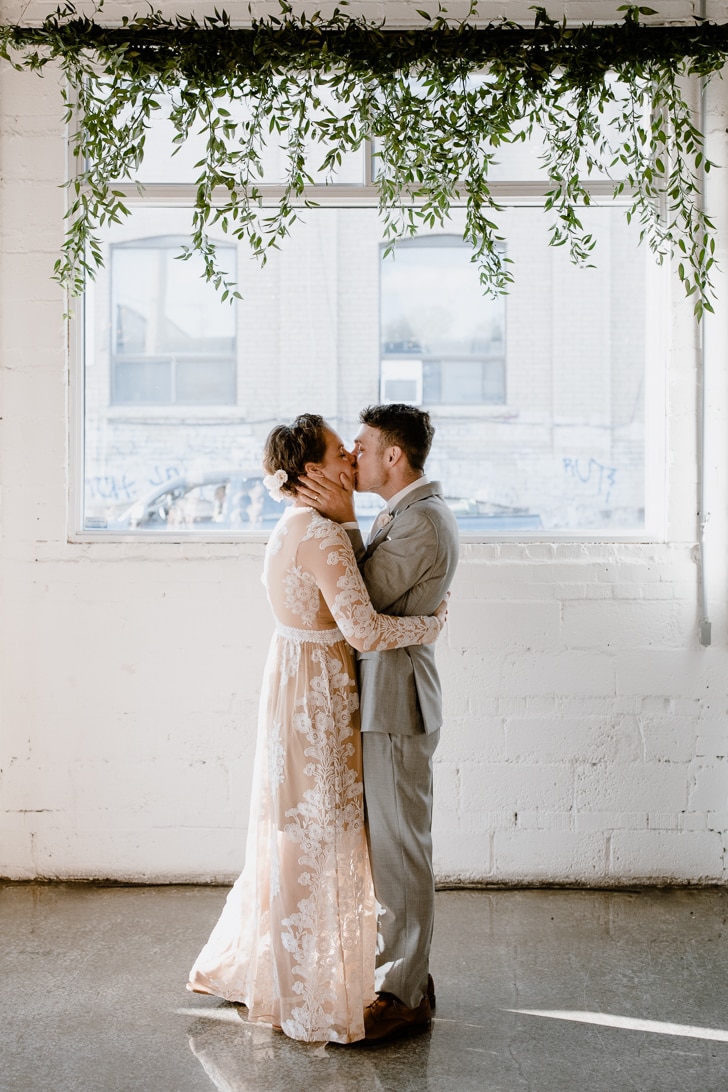 A bride and groom kiss in front of a window at their Propeller Coffee Co. wedding in Toronto.