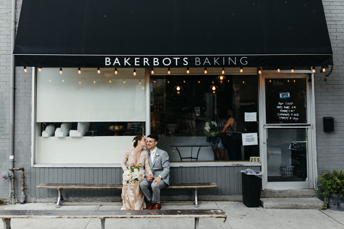 bride and groom sitting in front of bake shop Toronto_EightyFifth Street Photography