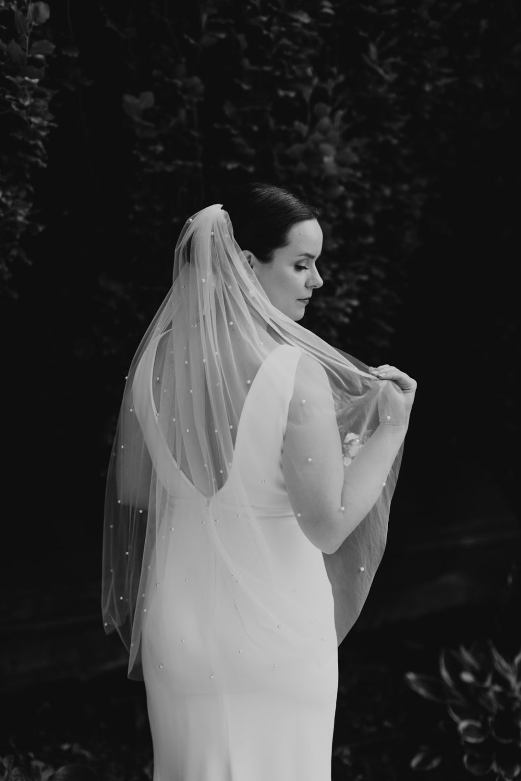 bride lifts veil with pearls over shoulder