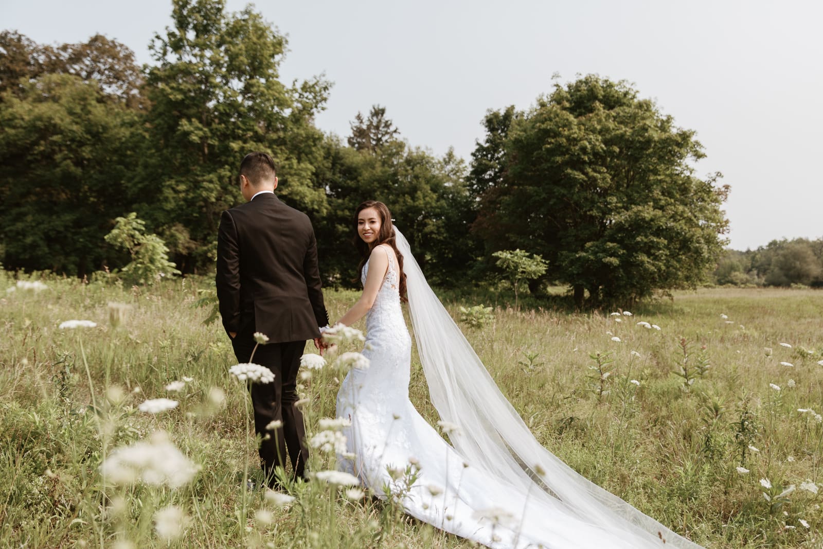 A bride and groom enjoying their romantic stroll through a beautiful field of wildflowers at Scotsdale farm in Caledon Ontario.