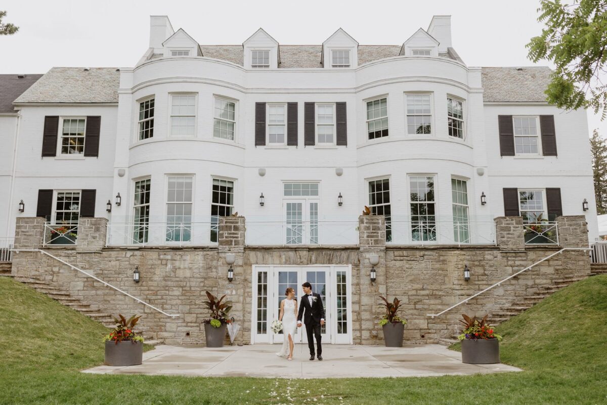 A bride and groom standing in front of the Harding Waterfront Estate on their wedding day.