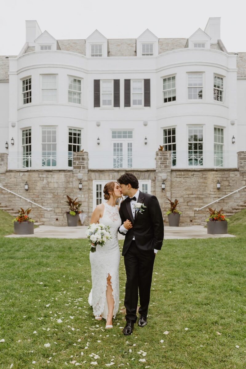 A bride and groom kiss in front of Harding Waterfront Estate on their wedding day.