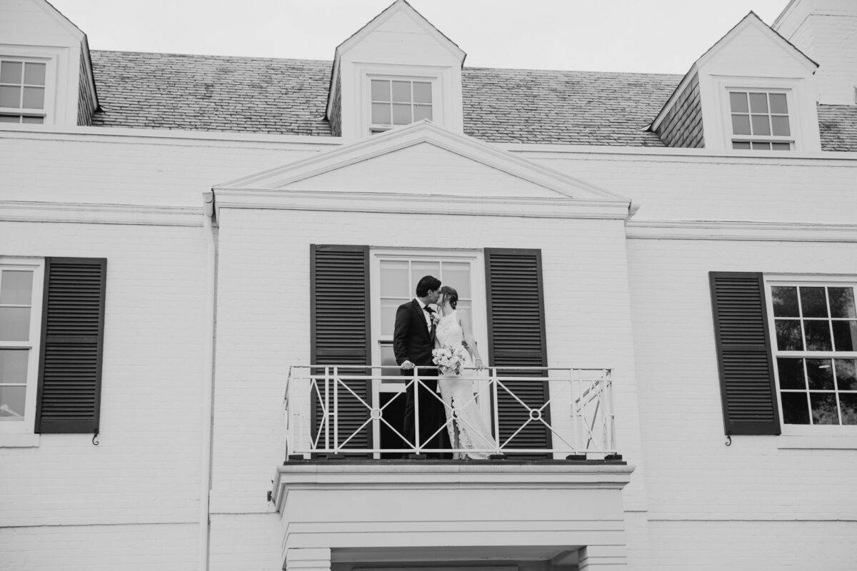 A bride and groom share an intimate kiss on the balcony of the mansion at Harding Waterfront Estate during their wedding celebration.