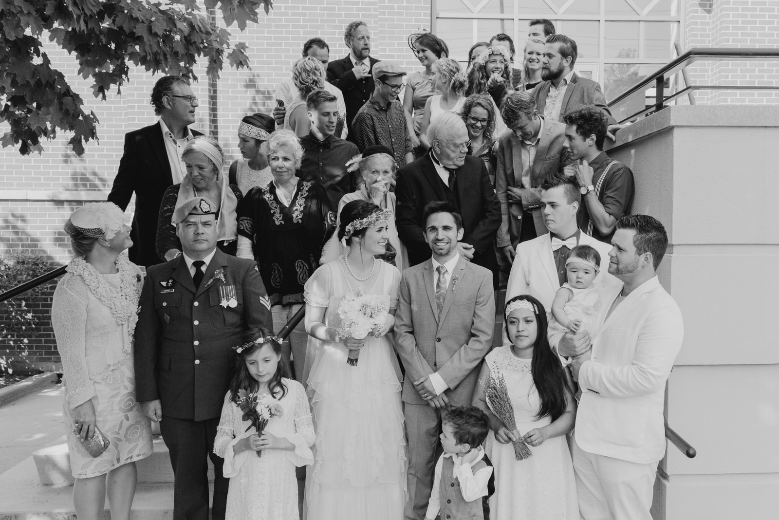 A black and white photograph of a diverse wedding family gathered on steps of a church for a family wedding photo, with the bride and groom in the center.